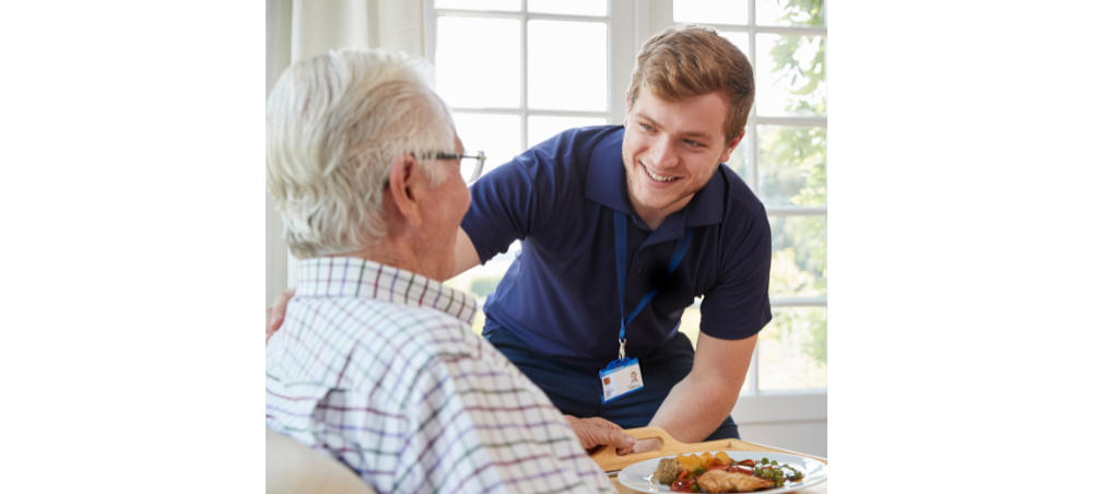 CAH short shift campaign A young caregiver brings a meal to an elderly man.