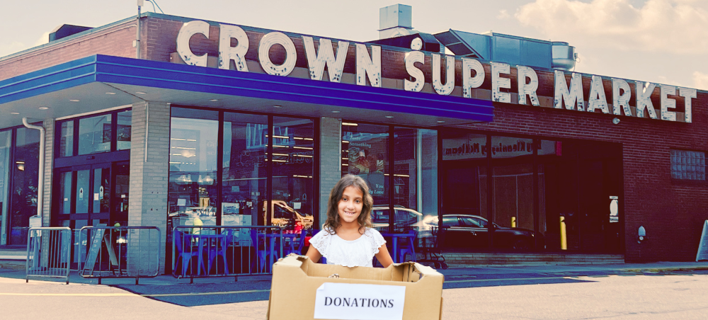 People Need Help Sometimes A young girl stands in front of The Crown Market holding a donation box.